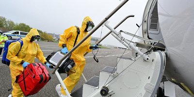 Rettungsdienst-Mitarbeitende in gelben Schutzanzügen betreten das Flugzeug