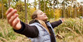 Mädchen mit ausgestreckten Armen im Wald bei einer Yoga Atemübung zur Entspannung