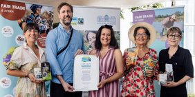 Fünf Menschen auf einer Bühne im Schlossgarten, die die Fairtrade-Urkunde und faire Produkte in die Kamera halten