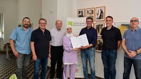 Regionalverbandsdirektor Peter Gillo überreicht an mehrere Mitglieder des Kulturvereins Burbach ein Förderschreiben für das Projekt "Hier daheim"