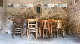 Bilder und Texte der Ausstellung zur Regionalen Baukultur an der Wand der Alten Scheune des Jagdschlosses Karlsbrunn. Im Raum stehen auch mehrer alte Stühl die zum Betrachten der Bilder einladen