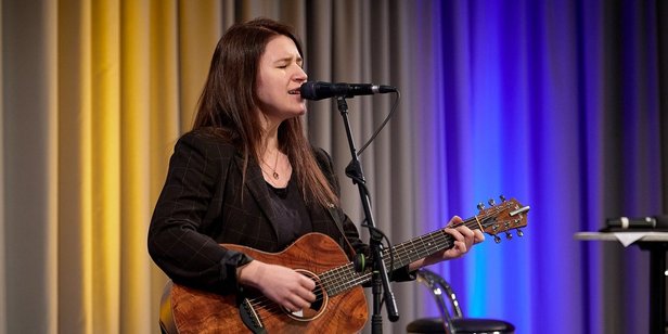 Die Preisträgerin Isabell Krohn (EASY) trat zunächst solo mit Gitarre auf. Foto: Kerstin Krämer Die Sängerin Isabell Krohn tritt mit Gitarre auf der Bühne des Festsaals auf. Sie hat langes, dunkles glattes Haar und trägt einen schwarz-karierten Blazer.
