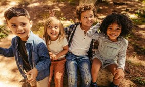 vier glückliche Kinder sitzen auf Baumstamm in einem Wald