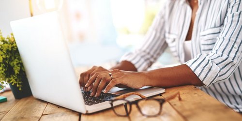 Junge Frau an einem Holztisch die etwas am Laptop eingibt