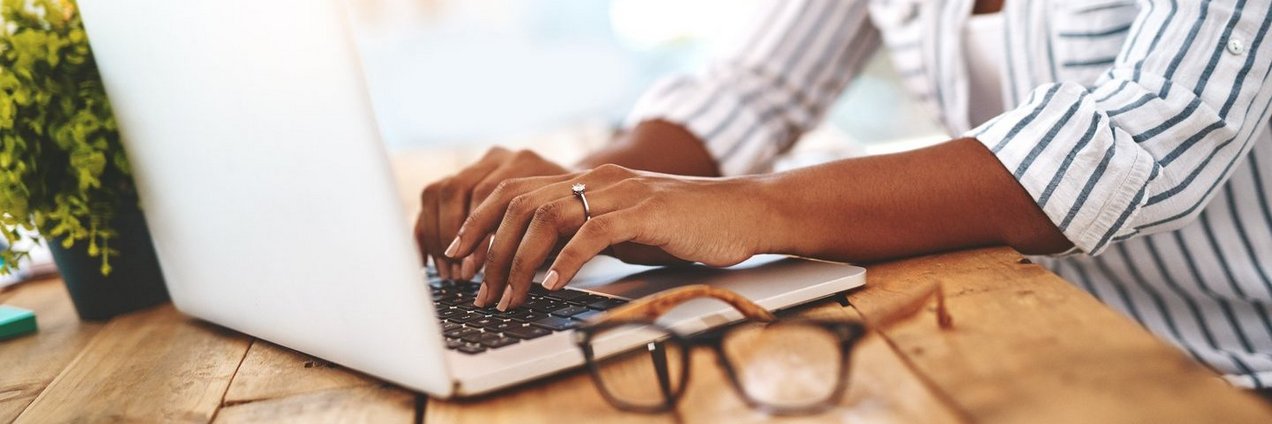 Junge Frau an einem Holztisch die etwas am Laptop eingibt