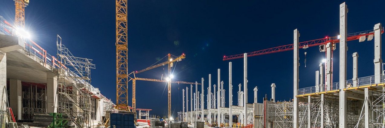 Baustelle mit diversen Baukränen bei Nacht