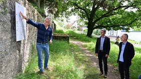 Peter Michael Lupp, Kulturreferent des Regionalverbandes, erläutert an Hand eines Schildes an einer restaurierten Sandsteinmauer Regionalverbandsdirektor Peter Gillo sowie Rainer Lang, Bürgermeister von Kleinblittersdorf, und Ortsvorsteher Karl Peter Fuhr die kultur- und baugeschichtliche Bedeutung des Pasquay-Geländes