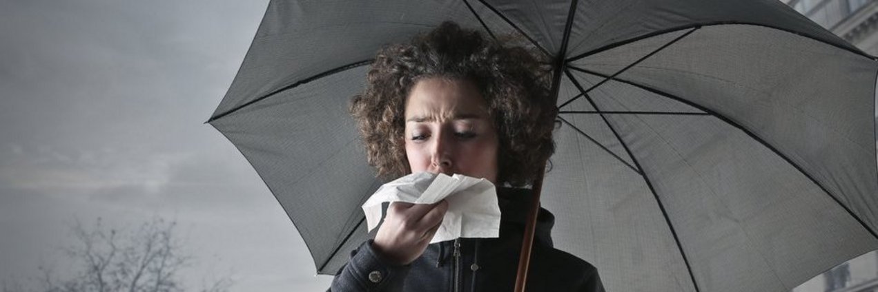 Eine Frau mit Regenschirm schnäutzt in ein Taschentuch