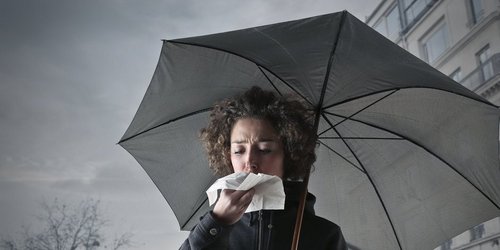 Eine Frau mit Regenschirm schnäutzt in ein Taschentuch