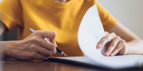 Eine Frau unterschreibt ein Dokument; ihre Hand hält einen Stift und setzt die Unterschrift auf das Dokument.