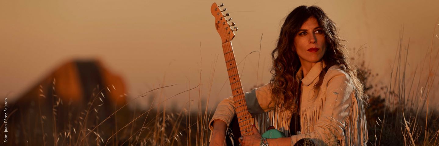 Die Musikerin Susan Santos ist in abendlicher Stimmung auf einer Wiese mit ihrer Gitarre