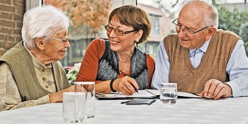 Ein Seniorenpaar wird von einer Frau am Tisch sitzend beraten