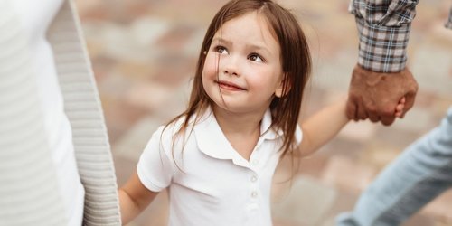 Mädchen hält die Hände ihrer Eltern und blickt zur Mutter hoch. 