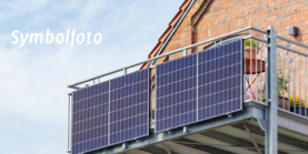 Ein Balkon an einem Backsteinhaus. Am Balkon sind die Solarpanele eines Balkonkraftwerks befestigt. Auf dem Bild steht Symbolfoto geschrieben