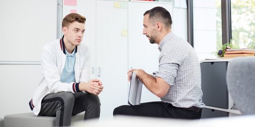 ein Mann sitzt mit einem Jugendlichen in seinem Büro bei einem Gespräch