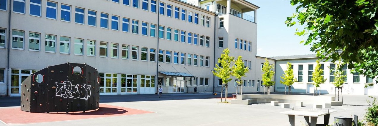 Schulhof mit Kletterwand, Bäumen und Tischtennisplatte vor dem Gebäude des Ludwigsgymnasium Saarbrücken