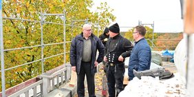 Der Erste Regionalverbandsbeigeordnete Norbert Moy und Bauamtsmitarbeiter Giuseppe Messina stehen auf dem Dach der Graf-Ludwig-Gemeinschaftsschule in Ludweiler und sprechen mit mehreren Männern einer Dachdeckerfirma, die dort gerade Sanierungsarbeiten vornimmt.