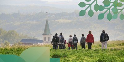 Eine Wandergruppe von hinten aufgenommen, die ins Tal mit einer Kirche hineinwandert.