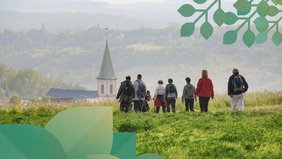 Eine Wandergruppe von hinten aufgenommen, die ins Tal mit einer Kirche hineinwandert.