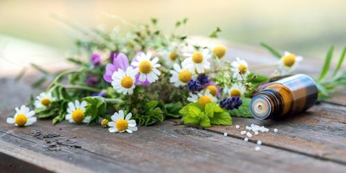 Wildblumenstrauß auf einem Holztisch und nebenan liegt ein Fläschen Globuli