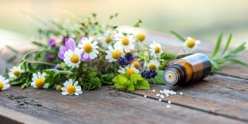 Wildblumenstrauß auf einem Holztisch und nebenan liegt ein Fläschen Globuli