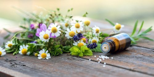 Wildblumenstrauß auf einem Holztisch und nebenan liegt ein Fläschen Globuli