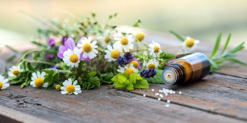 Wildblumenstrauß auf einem Holztisch und nebenan liegt ein Fläschen Globuli