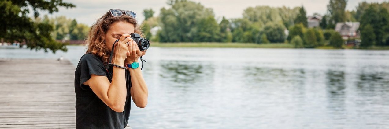 Frau fotografiert Frau an Flussufer beziehungsweise Steg am Fotografieren