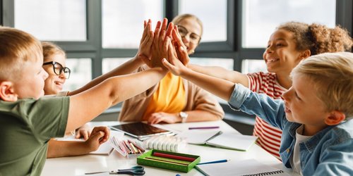 Kinder geben sich High Five an einem Tisch mit Arbeitsmaterialien