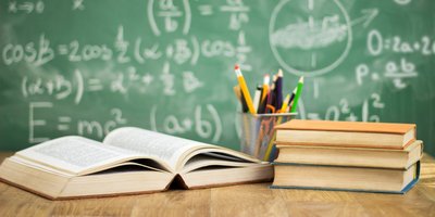 Schulbücher und Stifte vor einr Tafel mit Mathematischen Formeln