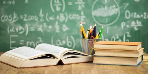 Schulbücher und Stifte vor einr Tafel mit Mathematischen Formeln