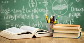 Schulbücher und Stifte vor einr Tafel mit Mathematischen Formeln