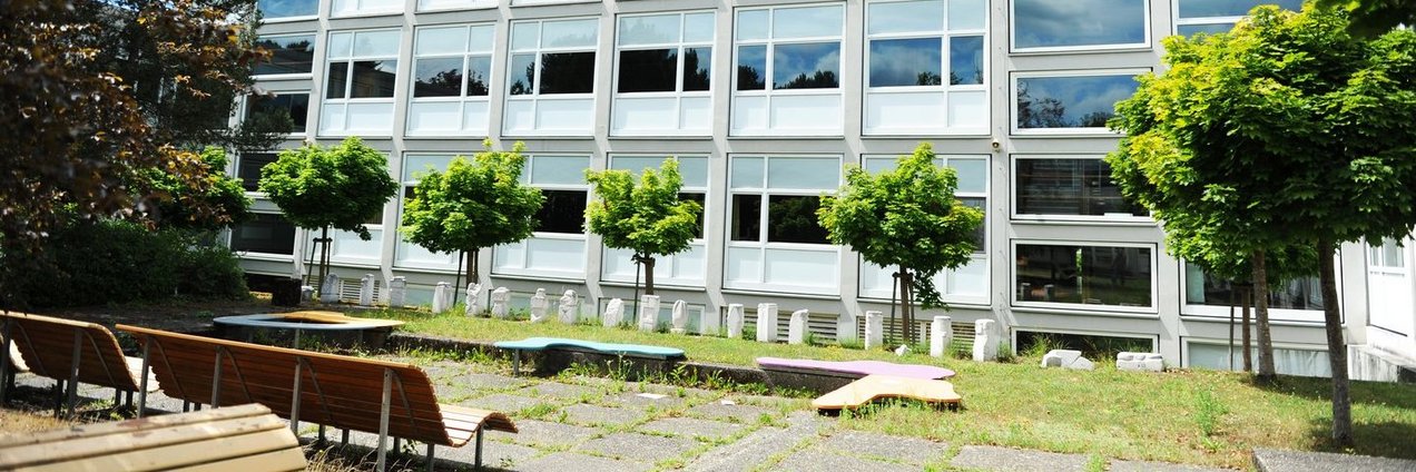 Schulhof mit Bänken und Bäumen vor dem Schulgebäude des Rotenbühl Gymnasium Saarbrücken