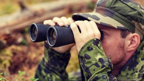 Ein Soldat schaut im Wald durch ein Fernglas