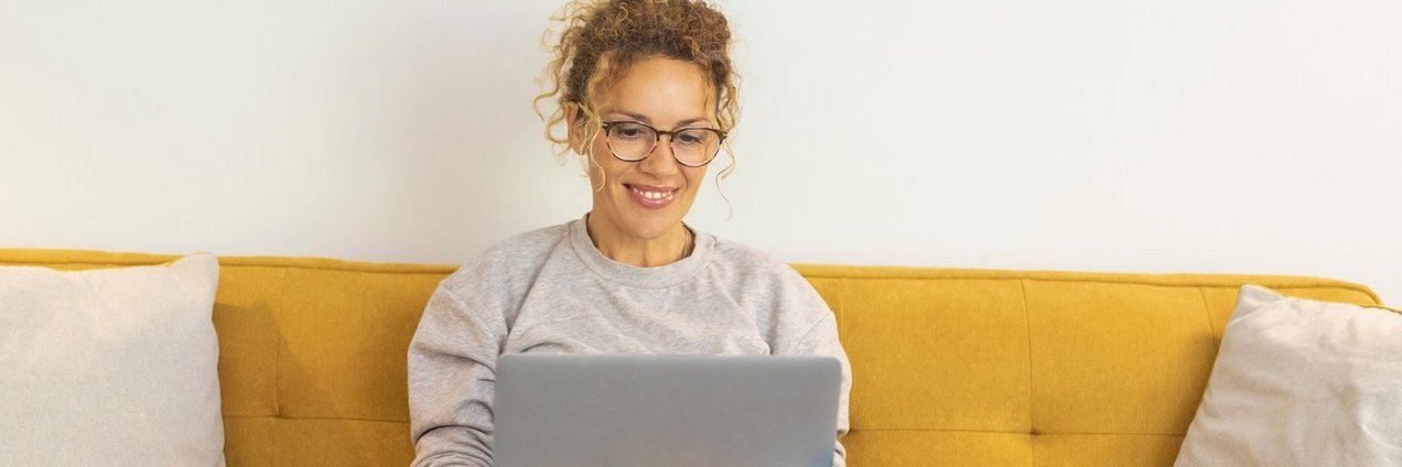 Frau sitzt mit einem Laptop auf dem Schoß auf der Couch