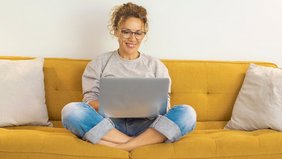 Frau sitzt mit einem Laptop auf dem Schoß auf der Couch