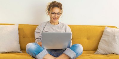 Frau sitzt mit einem Laptop auf dem Schoß auf der Couch