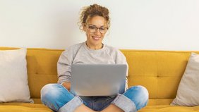 Frau sitzt mit einem Laptop auf dem Schoß auf der Couch
