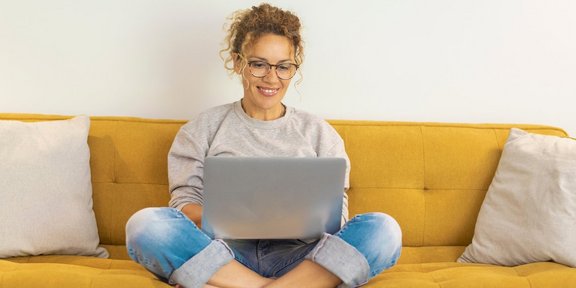 Frau sitzt mit einem Laptop auf dem Schoß auf der Couch