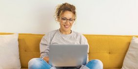 Frau sitzt mit einem Laptop auf dem Schoß auf der Couch