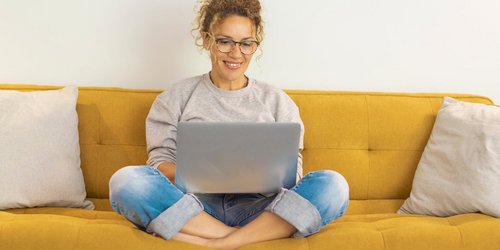 Frau sitzt mit einem Laptop auf dem Schoß auf der Couch