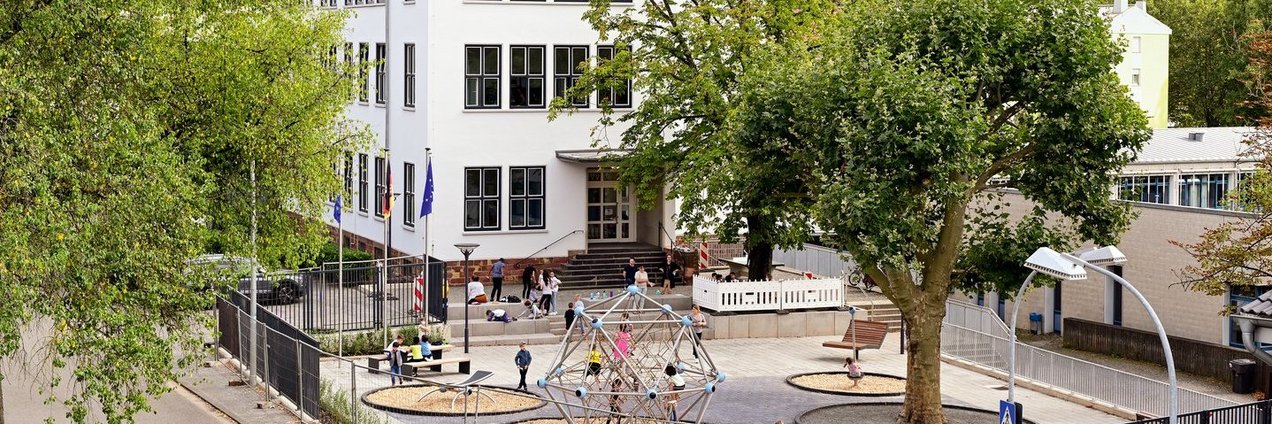 Schulgebäude und Schulhof mit Klettergerüst, Bänken und Spielgeräten der Europa Schule Saarbrücken