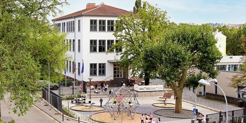 Schulgebäude und Schulhof mit Klettergerüst, Bänken und Spielgeräten der Europa Schule Saarbrücken