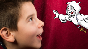 Ein Junge schaut aus einem roten Bühnenvorhang hervor und blickt auf ein gezeichnetes fliegendes Schlossgespenst
