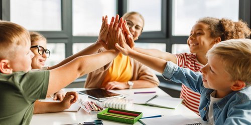 Lehrer sitzt mit Schülern an einem Tisch, freuen sich und klatschen ab