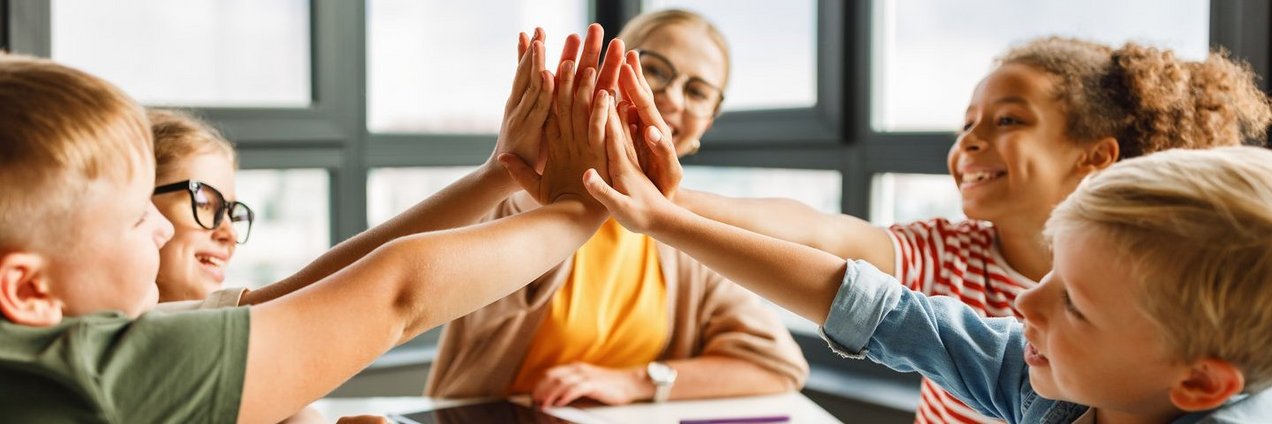 Lehrer sitzt mit Schülern an einem Tisch, freuen sich und klatschen ab