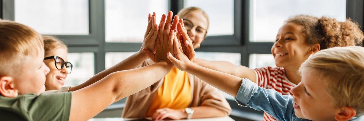 Lehrer sitzt mit Schülern an einem Tisch, freuen sich und klatschen ab