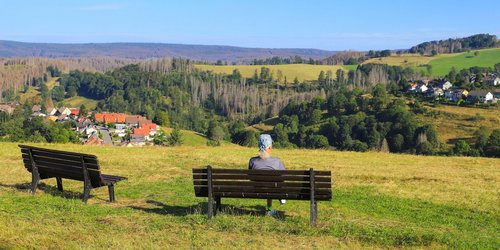 Mann sitzt auf einer Bank und schaut in ein Dorf im Tal