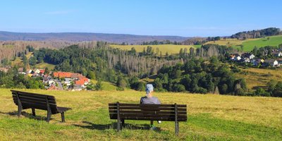 Mann sitzt auf einer Bank und schaut in ein Dorf im Tal